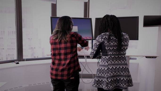 Das Bild zeigt zwei Personen arbeitend vor zwei Monitoren
