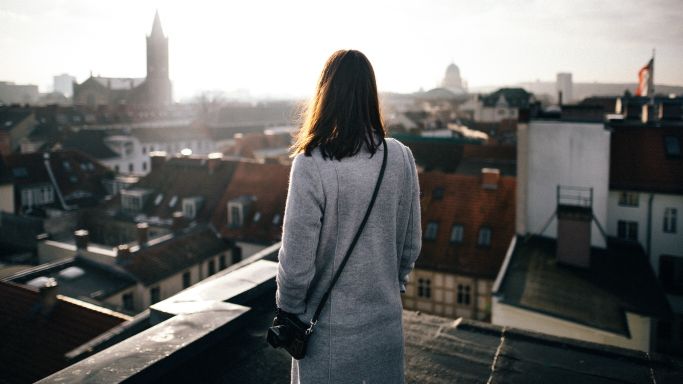 Das Bild zeigt eine Frau mit Kamera über einem Dächerpanorama.