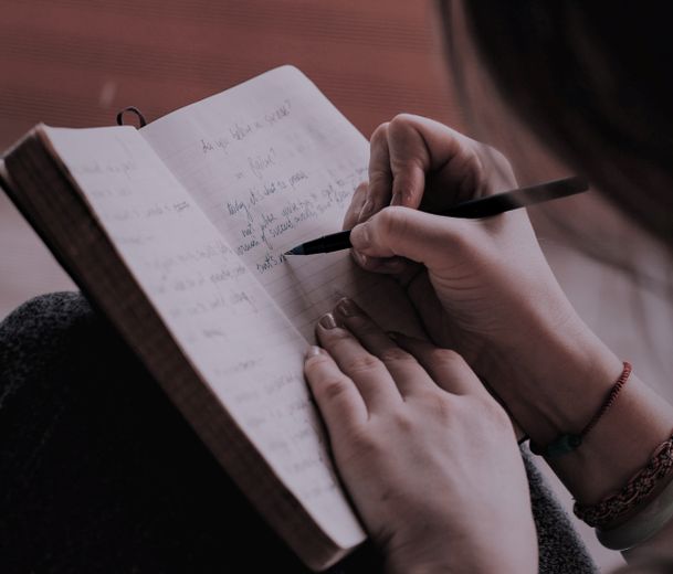 Das Bild zeigt eine Person, die in ein Notizbuch schreibt (Quelle: Marcus Paulo Prado - unsplash) Das Bild zeigt eine Person, die in ein Notizbuch schreibt