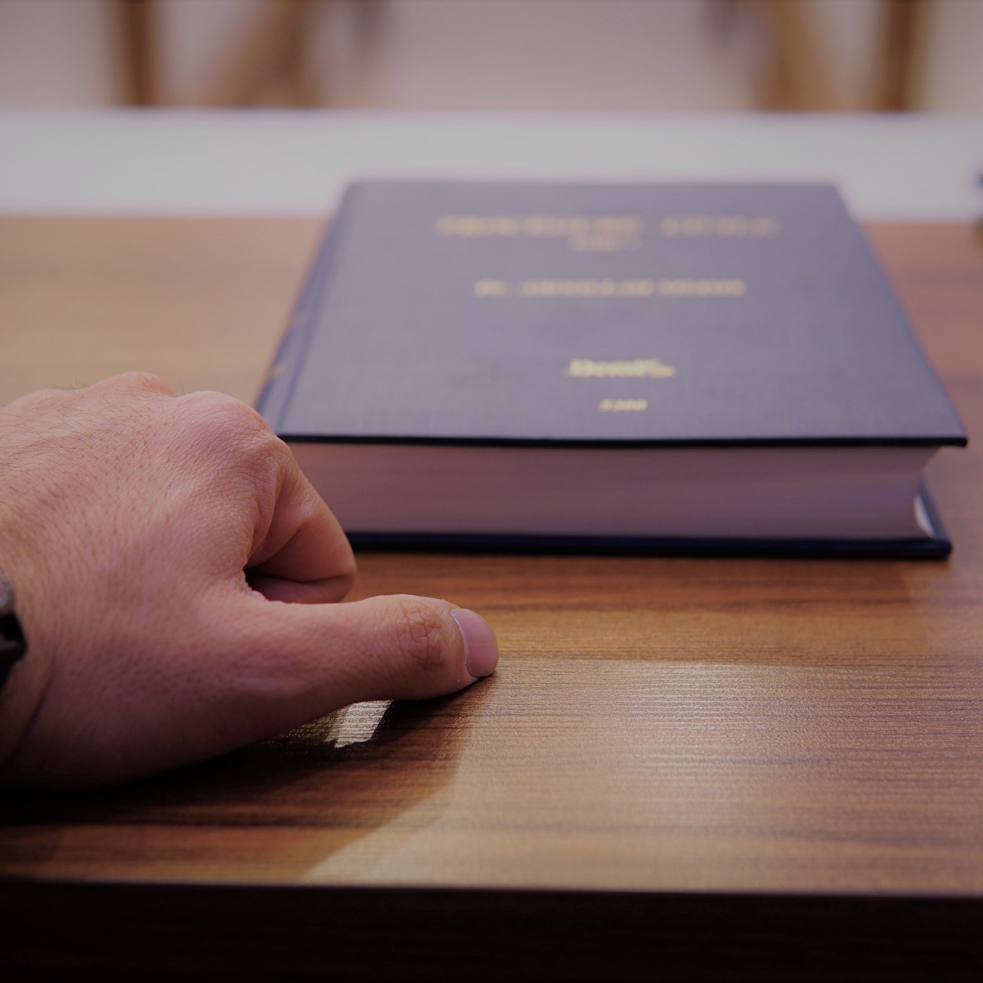 Das Bild zeigt die Hand einer männlichen Person auf einem Holztisch. Davor liegt ein Buch. (Quelle: moj-taba-hoseini-U69WqLoFGD4/Unsplash) Das Bild zeigt die Hand einer männlichen Person auf einem Holztisch. Davor liegt ein Buch.