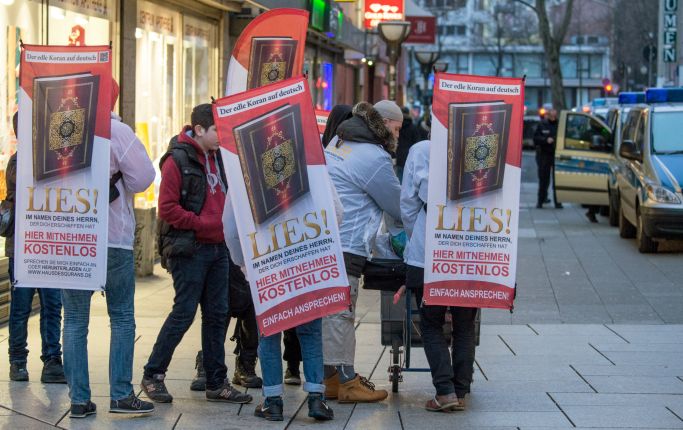 Die Aufnahme zeigt Personen mit Transparenten zur "Lies!"-Kampagne.  (Quelle: Picture Alliance/dpa/Boris Roessler) Die Aufnahme zeigt Personen mit Transparenten zur "Lies!"-Kampagne.
