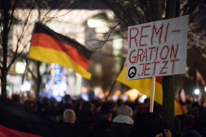 Teilnehmer einer Mahnwache rechter Gruppen stehen am 21.12.2016 mit einem Schild mit der Aufschrift "Remigration Jetzt" vor dem Bundeskanzleramt in Berlin. (Quelle: picture alliance / Bernd von Jutrczenka/dpa | Bernd von Jutrczenka) Teilnehmer einer Mahnwache rechter Gruppen stehen am 21.12.2016 mit einem Schild mit der Aufschrift "Remigration Jetzt" vor dem Bundeskanzleramt in Berlin.
