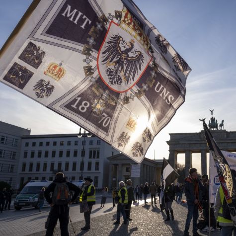 Die Aufnahme zeigt ein Demonstrationsgeschehen vom 14. März 2020 am Brandenburger Tor in Berlin, auf dem eine Flagge mit für die Reichsbürgerszene typischer Symbolik geschwenkt wird.