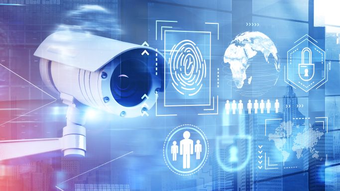 DIe Aufnahme zeigt eine CCTV Kamera in 3D-Optik mit einem städtischen Hintergrund und einen projizierten Cybersicherheits-Interface daneben (Quelle: ismagilov / iStock / Getty Images Plus) DIe Aufnahme zeigt eine CCTV Kamera in 3D-Optik mit einem städtischen Hintergrund und einen projizierten Cybersicherheits-Interface daneben