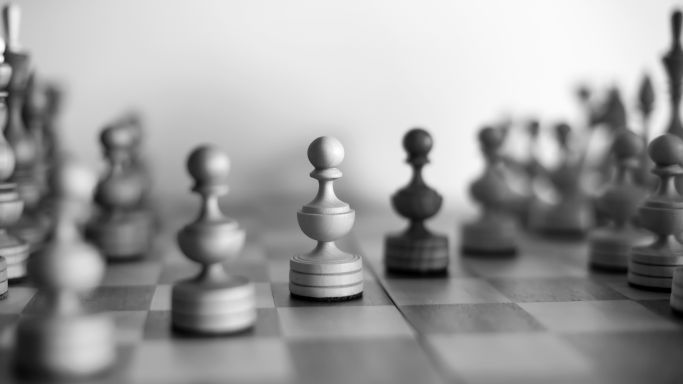 Die Aufnahme zeigt ein Schachbrett, auf dem sich weiße und schwarze Figuren in einer Partie gegenüber stehen