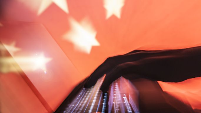 Die Abbildung zeigt einen im Verborgenen agierenden Hacker mit der Silhouette der chinesischen Flagge im Hintergrund