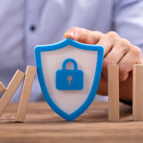Die Aufnahme zeigt einen Mann, der ein Sicherheitsschild aufrecht stehen lässt und hierdurch verhindert, dass eine Reihe von Dominosteinen fällt (Quelle: Andrey Popov / iStock / Getty Images Plus) Die Aufnahme zeigt einen Mann, der ein Sicherheitsschild aufrecht stehen lässt und hierdurch verhindert, dass eine Reihe von Dominosteinen fällt