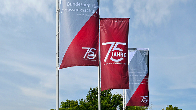 Das Bild zeigt drei Flaggen mit der Aufschrift „75 Jahre im Auftrag der Demokratie“ (Quelle: Bundesamt für Verfassungsschutz) Das Bild zeigt drei Flaggen mit der Aufschrift „75 Jahre im Auftrag der Demokratie“