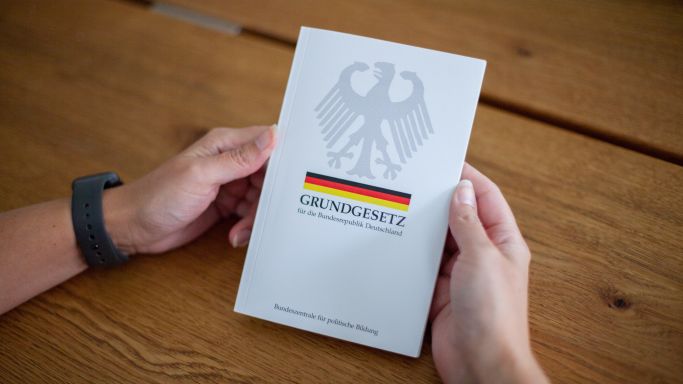 Die Aufnahme zeigt die Hände eines Mannes, die ein Grundgesetz halten