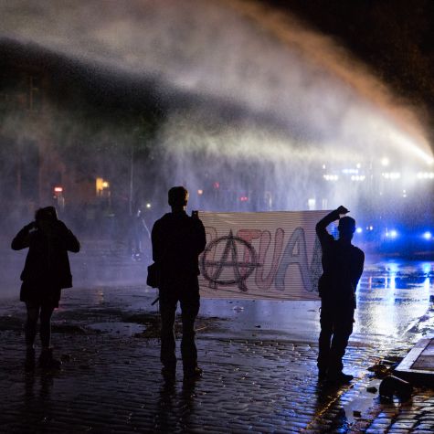 Activists hold a banner showing an anarchist symbol at night in Hamburg.