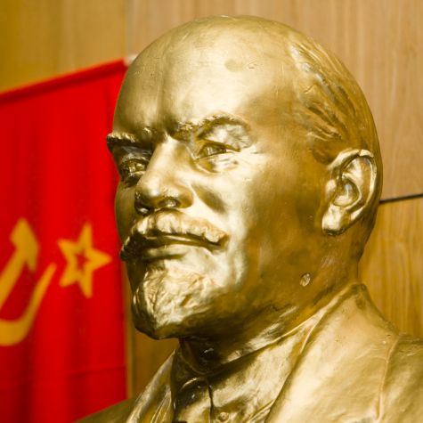 The photo shows a bust of Vladimir Ilyich Lenin with the flag of the Soviet Union in the background